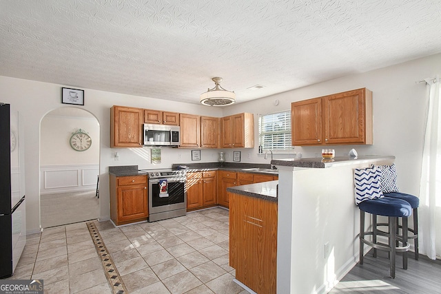 kitchen featuring dark countertops, appliances with stainless steel finishes, a kitchen breakfast bar, a peninsula, and a sink