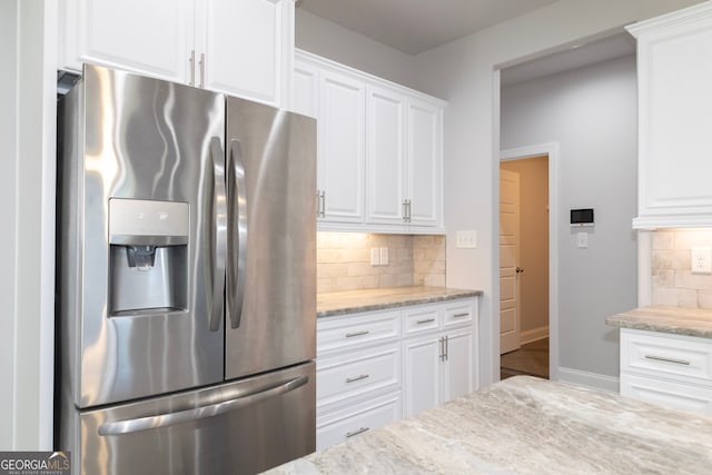 kitchen with light stone counters, white cabinetry, stainless steel refrigerator with ice dispenser, and tasteful backsplash