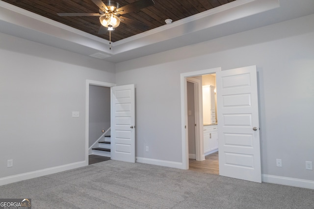 unfurnished bedroom with carpet, ornamental molding, a tray ceiling, ceiling fan, and wooden ceiling