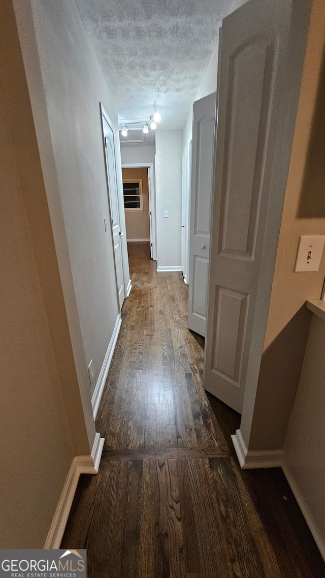 corridor with a textured ceiling and dark hardwood / wood-style floors