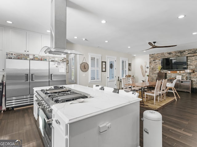 kitchen with white cabinetry, ceiling fan, dark wood-type flooring, light stone counters, and island range hood