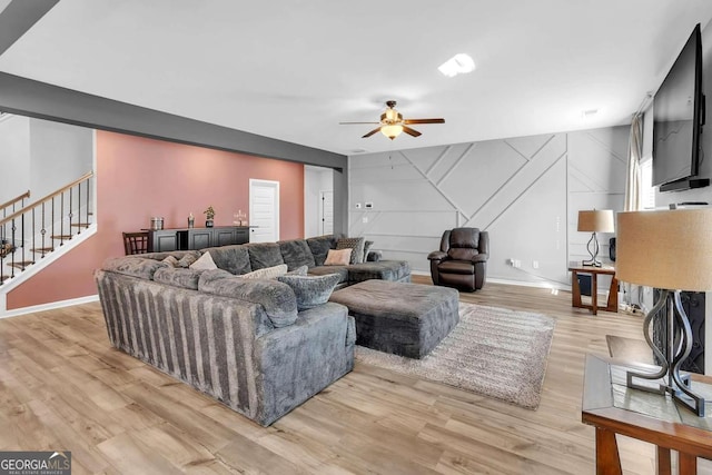 living area with stairs, light wood-type flooring, ceiling fan, and baseboards