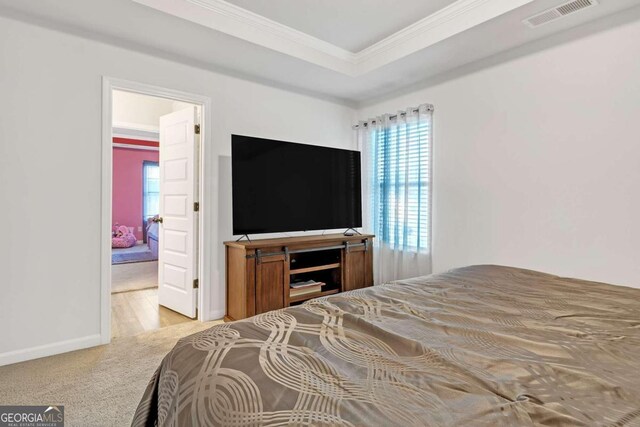 carpeted bedroom with baseboards, visible vents, crown molding, and a raised ceiling