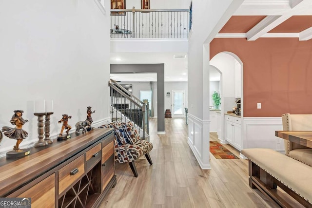 foyer featuring a wainscoted wall, stairs, light wood-style floors, arched walkways, and a towering ceiling