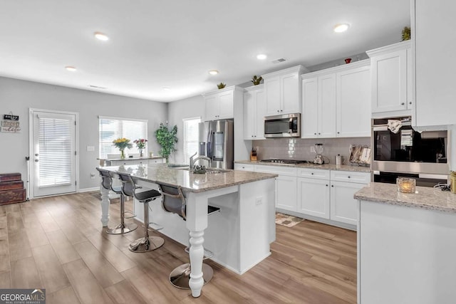 kitchen with decorative backsplash, white cabinets, a kitchen bar, and appliances with stainless steel finishes
