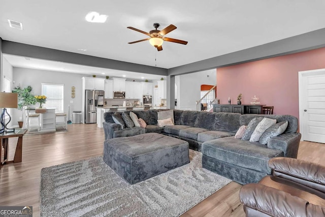 living room with stairs, light wood finished floors, ceiling fan, and visible vents