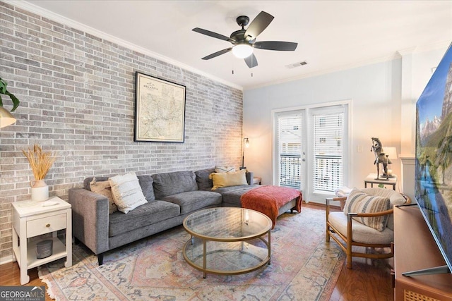 living room featuring hardwood / wood-style flooring, crown molding, and brick wall