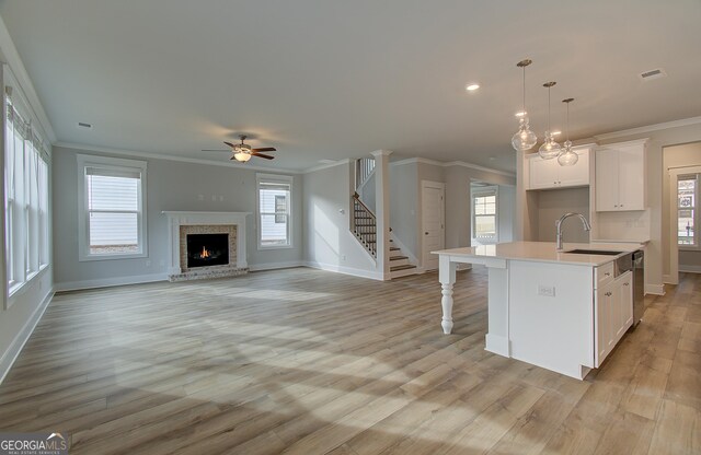 kitchen featuring white cabinets, crown molding, hanging light fixtures, ceiling fan, and an island with sink