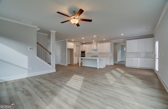 unfurnished living room featuring ceiling fan, sink, light wood-type flooring, and ornamental molding