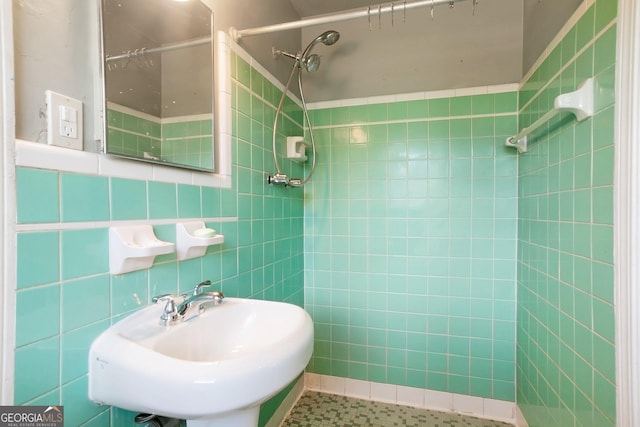 full bathroom with tiled shower, a sink, and tile walls