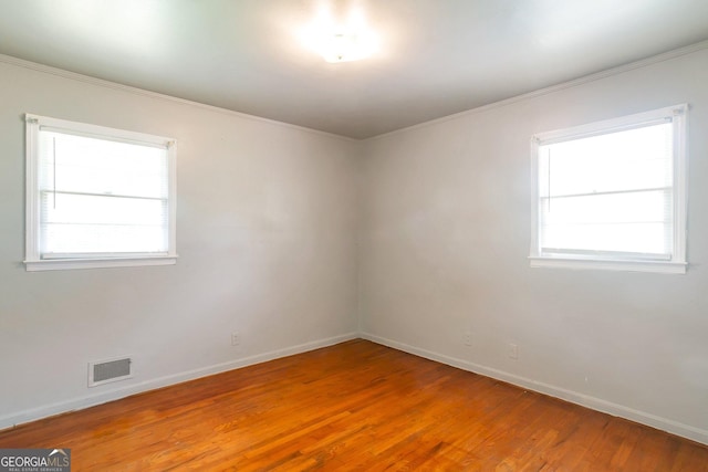 empty room with crown molding, light wood-type flooring, visible vents, and baseboards