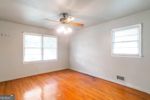 empty room with crown molding, visible vents, light wood-style floors, a ceiling fan, and baseboards