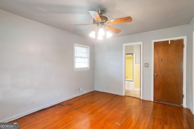 unfurnished bedroom with baseboards, visible vents, ensuite bath, ornamental molding, and wood finished floors