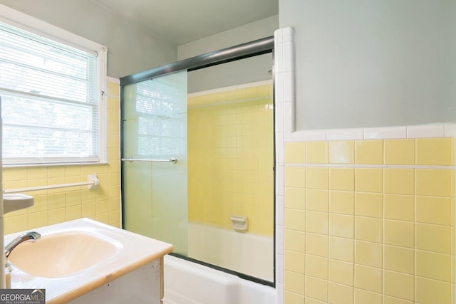 full bath featuring tile walls, vanity, and bath / shower combo with glass door