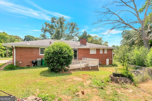 rear view of house featuring a deck, a yard, brick siding, and a chimney