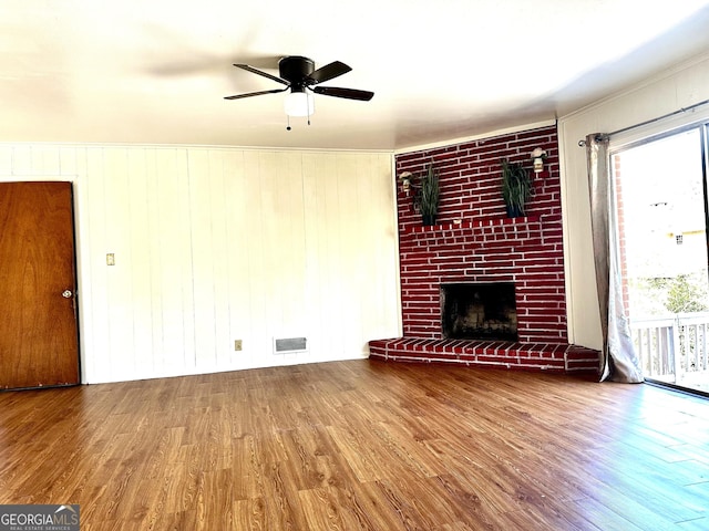 unfurnished living room featuring a brick fireplace, wood finished floors, visible vents, and a ceiling fan