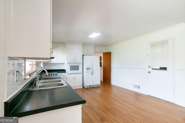 kitchen with white appliances, a sink, white cabinets, light wood finished floors, and dark countertops