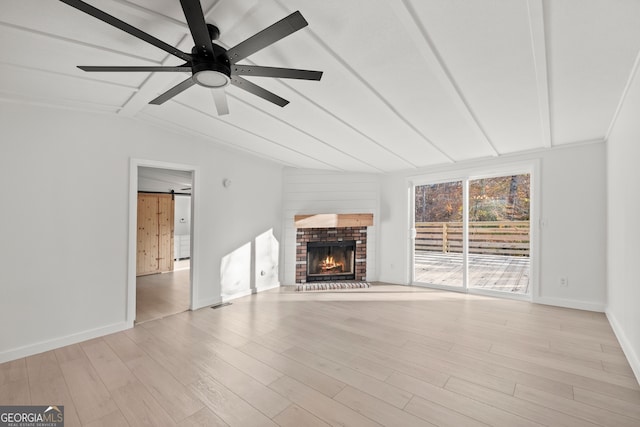 unfurnished living room featuring lofted ceiling, light hardwood / wood-style flooring, ceiling fan, a barn door, and a fireplace