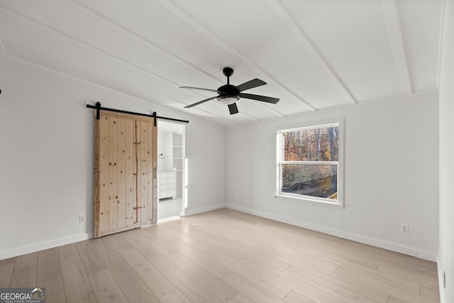 empty room with ceiling fan, a barn door, lofted ceiling with beams, and light hardwood / wood-style flooring