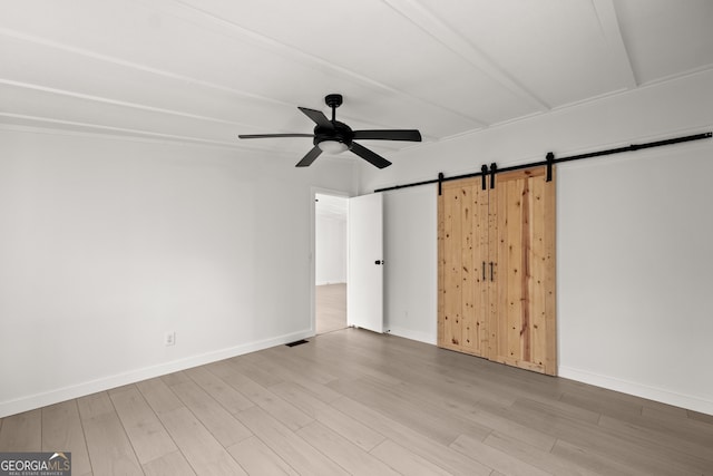 empty room featuring a barn door, hardwood / wood-style flooring, and ceiling fan