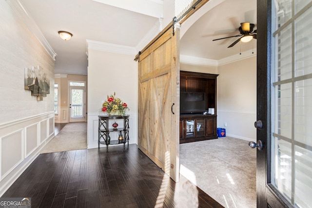 carpeted foyer with a barn door, crown molding, and ceiling fan