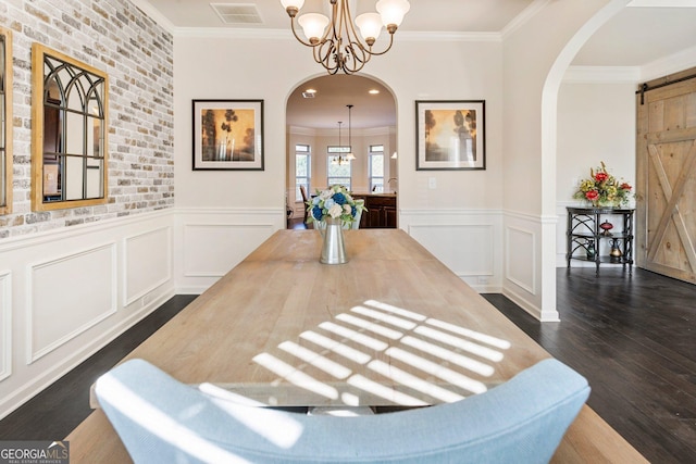 dining space with dark wood-type flooring, a barn door, brick wall, crown molding, and a chandelier