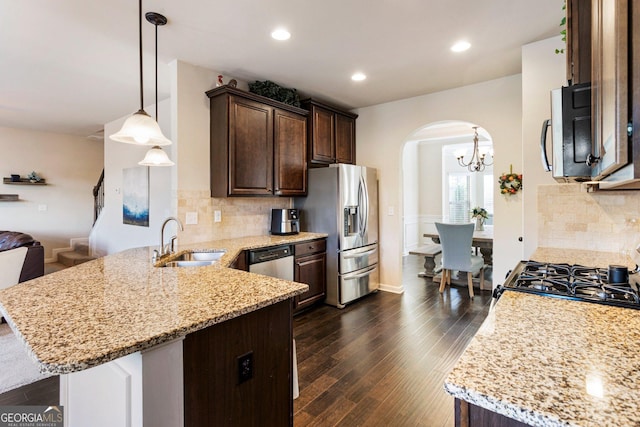 kitchen featuring kitchen peninsula, appliances with stainless steel finishes, dark wood-type flooring, sink, and hanging light fixtures