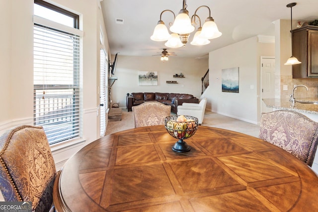 dining space featuring ceiling fan with notable chandelier, sink, and light carpet