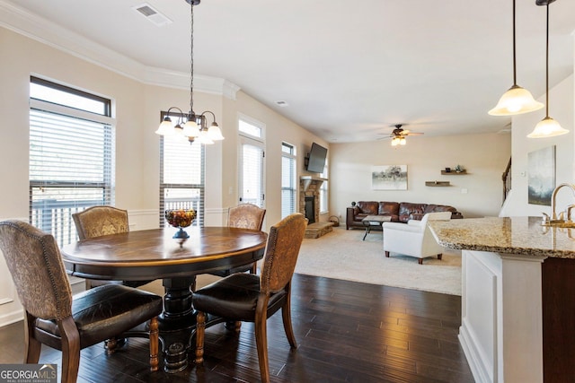 dining space featuring ceiling fan with notable chandelier, a stone fireplace, sink, crown molding, and dark hardwood / wood-style floors