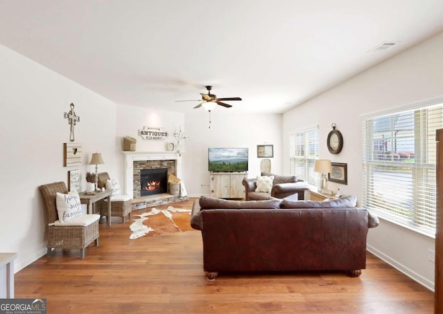 living room featuring hardwood / wood-style floors, a stone fireplace, and ceiling fan