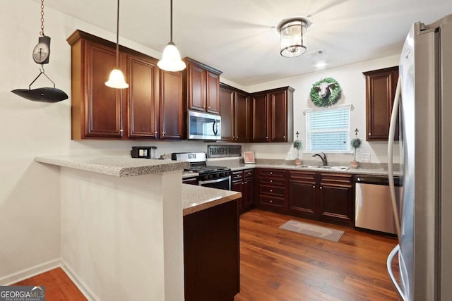 kitchen featuring kitchen peninsula, stainless steel appliances, dark wood-type flooring, sink, and pendant lighting