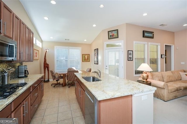 kitchen with a center island with sink, sink, vaulted ceiling, light tile patterned floors, and appliances with stainless steel finishes