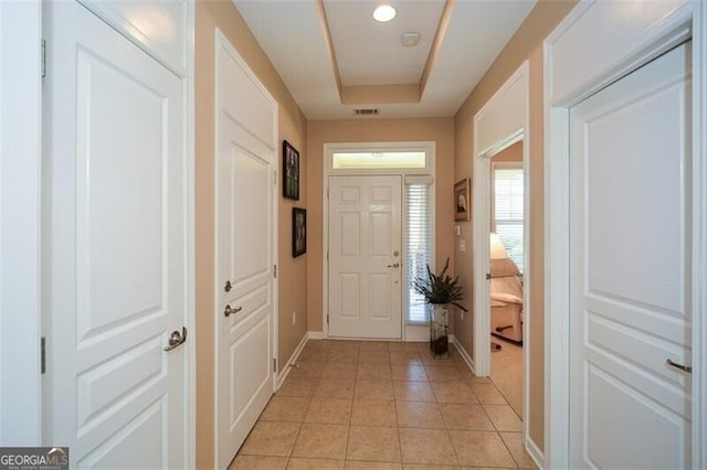 entryway with a raised ceiling and light tile patterned floors