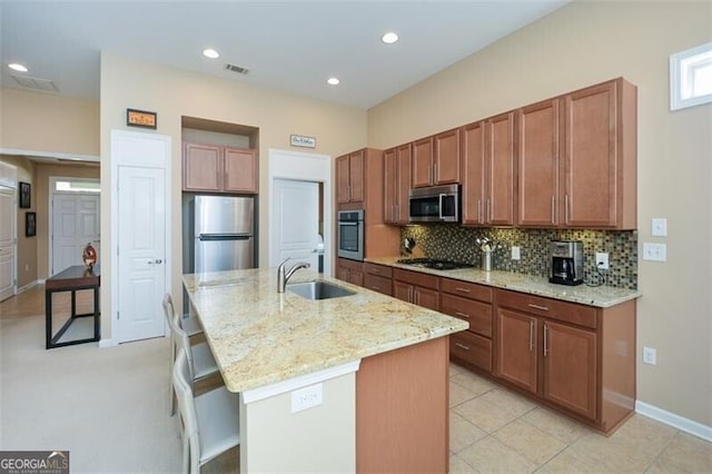 kitchen featuring sink, light stone counters, a center island with sink, light tile patterned flooring, and appliances with stainless steel finishes