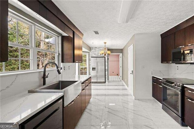 kitchen featuring sink, hanging light fixtures, light stone counters, a textured ceiling, and appliances with stainless steel finishes