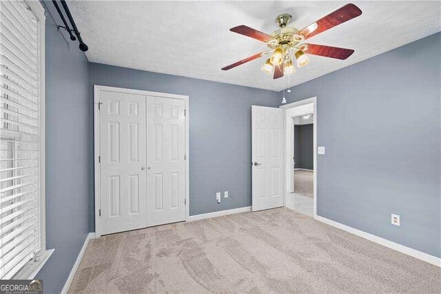 unfurnished bedroom with ceiling fan, a closet, light carpet, and a textured ceiling