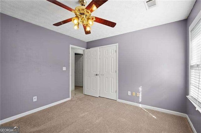 unfurnished bedroom featuring light carpet, a closet, multiple windows, and ceiling fan