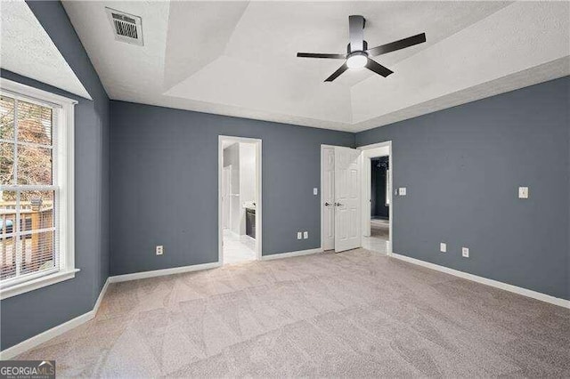 unfurnished bedroom featuring light carpet, a tray ceiling, ensuite bath, and ceiling fan