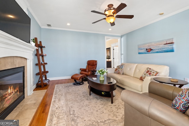 living room featuring a tile fireplace, crown molding, ceiling fan, and light hardwood / wood-style floors