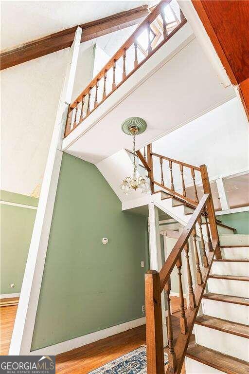 staircase featuring wood-type flooring, lofted ceiling, and a notable chandelier