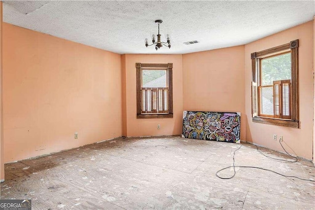 spare room with a healthy amount of sunlight, a textured ceiling, and a chandelier