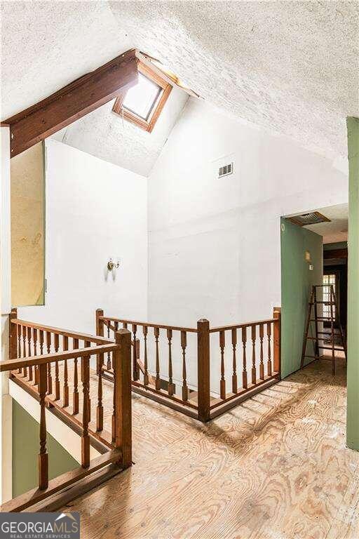 additional living space featuring hardwood / wood-style floors, a textured ceiling, and vaulted ceiling with skylight