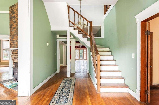 stairs featuring hardwood / wood-style floors, a high ceiling, and a brick fireplace