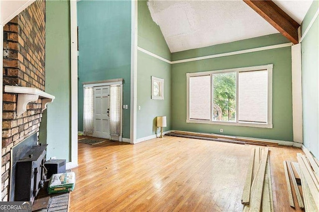 unfurnished living room with beam ceiling, a wood stove, hardwood / wood-style floors, and high vaulted ceiling