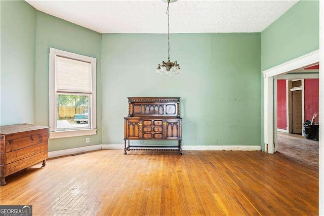 empty room with a chandelier, wood-type flooring, and a textured ceiling