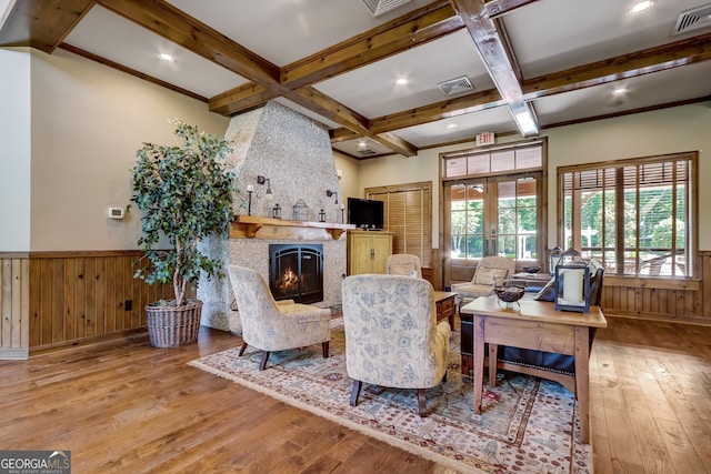 living room featuring beamed ceiling, a large fireplace, light hardwood / wood-style flooring, and wooden walls