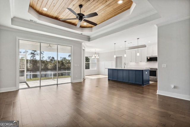 unfurnished living room with a raised ceiling, ceiling fan with notable chandelier, and dark hardwood / wood-style floors