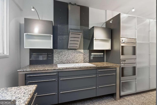 kitchen featuring backsplash, gray cabinets, light stone countertops, double oven, and cooktop