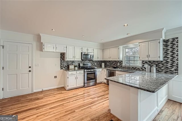 kitchen with kitchen peninsula, white cabinetry, dark stone countertops, and stainless steel appliances