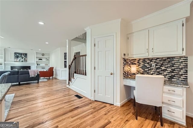 office with built in shelves, built in desk, ornamental molding, and light hardwood / wood-style flooring